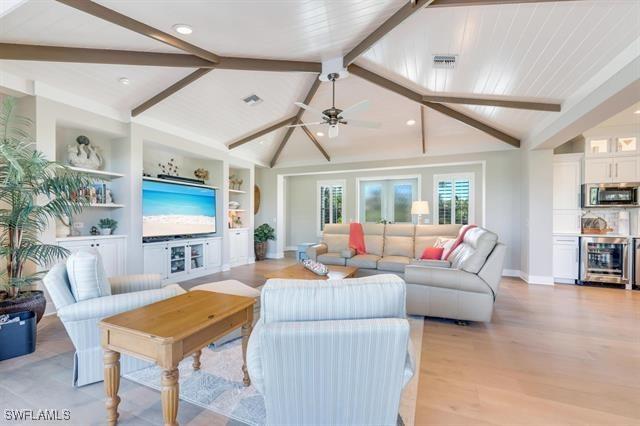 living room with lofted ceiling with beams, ceiling fan, built in shelves, light wood-type flooring, and beverage cooler