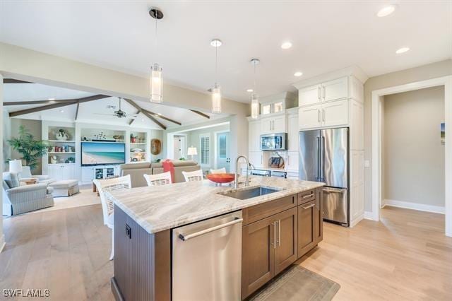 kitchen featuring light stone countertops, stainless steel appliances, sink, a center island with sink, and white cabinets