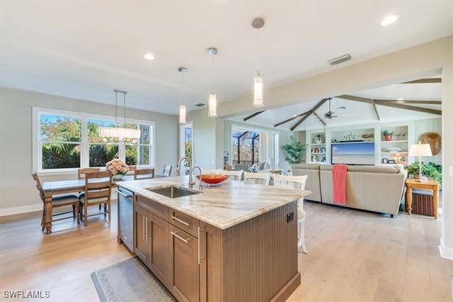 kitchen with stainless steel dishwasher, sink, pendant lighting, a center island with sink, and light hardwood / wood-style floors