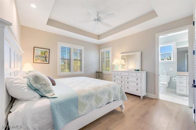 bedroom featuring light wood-type flooring, ensuite bathroom, a raised ceiling, and ceiling fan