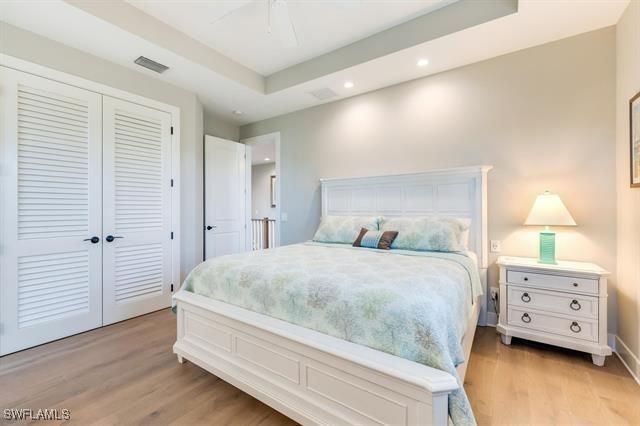 bedroom with a raised ceiling, a closet, ceiling fan, and light hardwood / wood-style flooring