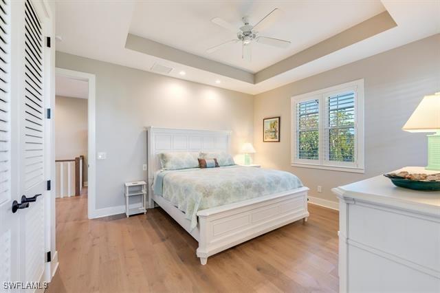 bedroom with a tray ceiling, ceiling fan, and light hardwood / wood-style flooring