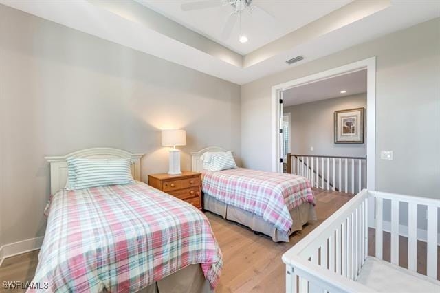 bedroom featuring ceiling fan, a raised ceiling, and light hardwood / wood-style flooring