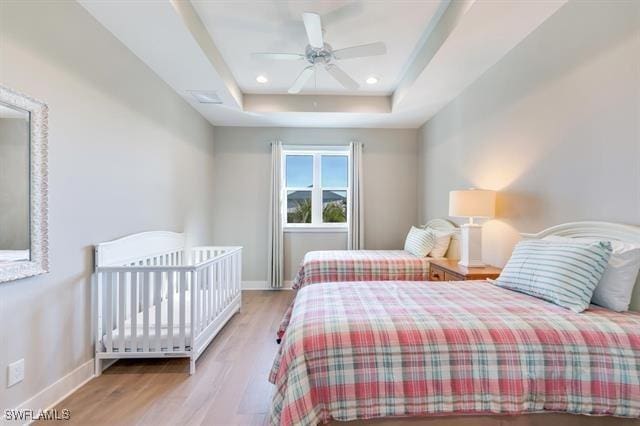 bedroom with ceiling fan, a tray ceiling, and light hardwood / wood-style flooring