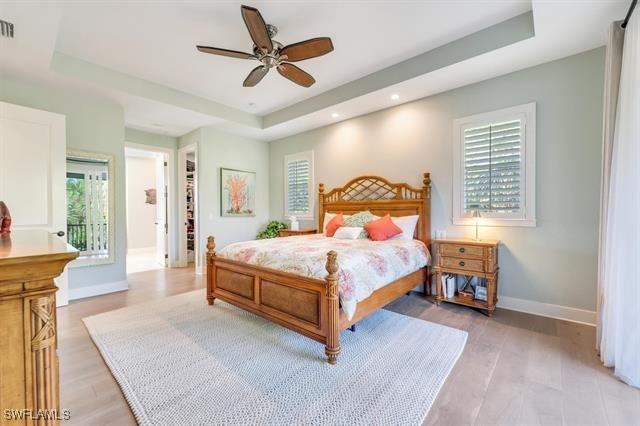 bedroom featuring a spacious closet, ceiling fan, light hardwood / wood-style floors, a tray ceiling, and a closet