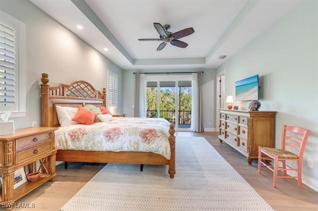 bedroom with ceiling fan, a tray ceiling, access to outside, and light hardwood / wood-style flooring