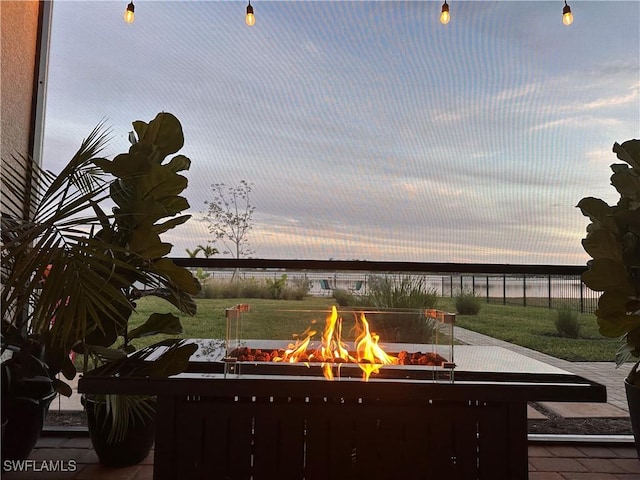 patio terrace at dusk featuring a lawn, a water view, and an outdoor fire pit