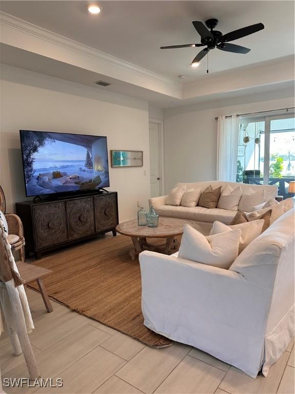 living room featuring ceiling fan, ornamental molding, and a tray ceiling