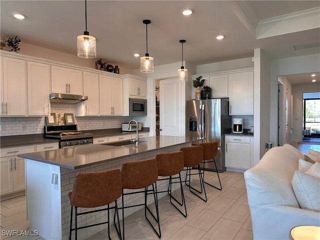 kitchen featuring stainless steel appliances, hanging light fixtures, a center island with sink, and sink