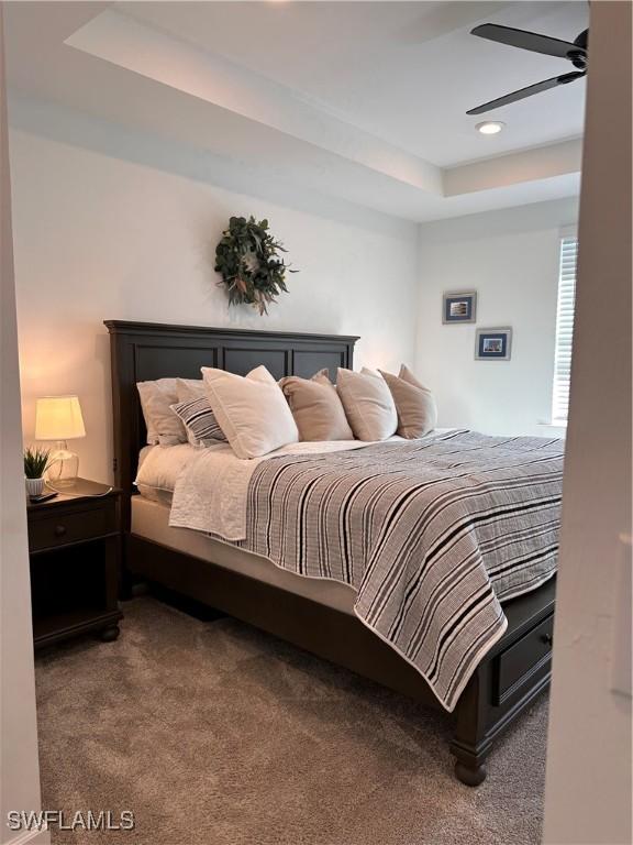 bedroom with a raised ceiling, ceiling fan, and carpet flooring