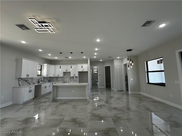 kitchen featuring backsplash, a kitchen island, sink, white cabinetry, and hanging light fixtures