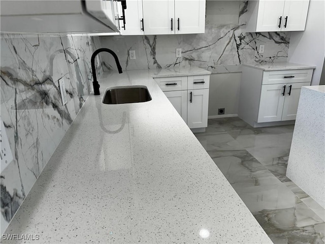 kitchen featuring white cabinets, decorative backsplash, light stone counters, and sink