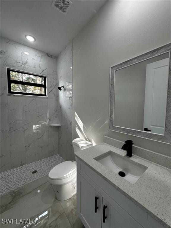 bathroom with a tile shower, vanity, and toilet