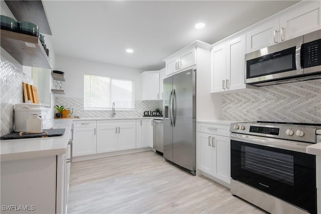 kitchen featuring appliances with stainless steel finishes, tasteful backsplash, sink, light hardwood / wood-style flooring, and white cabinets