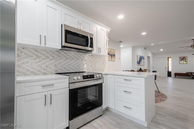 kitchen with stainless steel appliances, tasteful backsplash, kitchen peninsula, white cabinets, and light wood-type flooring