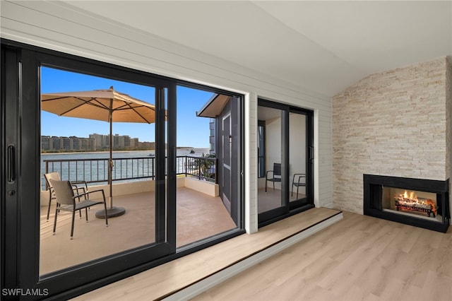 doorway to outside featuring light hardwood / wood-style floors, vaulted ceiling, a stone fireplace, and a water view