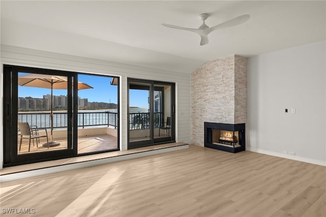 unfurnished living room featuring light wood-type flooring, ceiling fan, a water view, a multi sided fireplace, and lofted ceiling