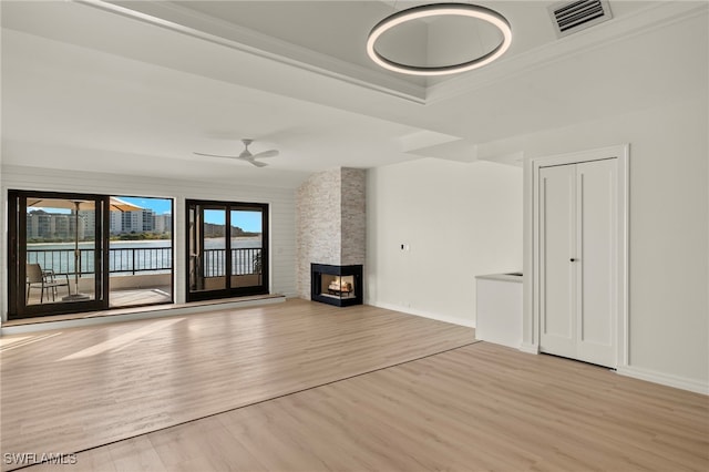 unfurnished living room featuring ceiling fan, light wood-type flooring, a fireplace, a water view, and ornamental molding