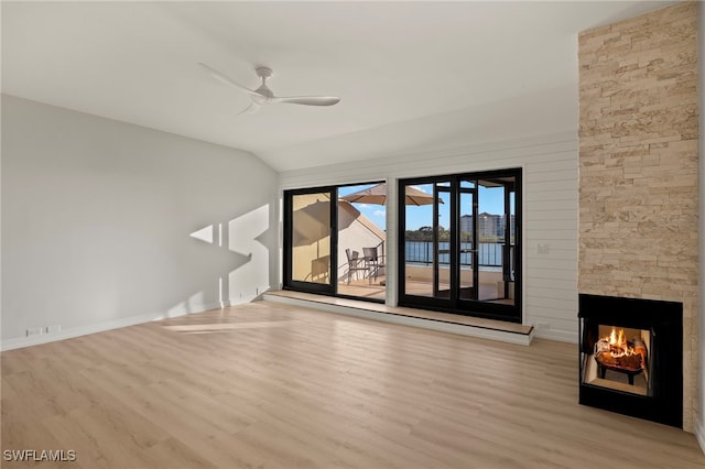 unfurnished living room featuring light hardwood / wood-style floors, a stone fireplace, ceiling fan, and lofted ceiling