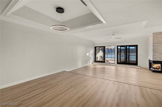 unfurnished living room with a multi sided fireplace, light hardwood / wood-style floors, a raised ceiling, and ceiling fan