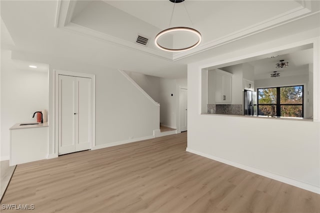 unfurnished living room with a tray ceiling, light hardwood / wood-style flooring, and sink