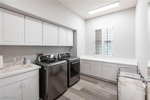 washroom featuring washer and clothes dryer, sink, cabinets, and light hardwood / wood-style floors