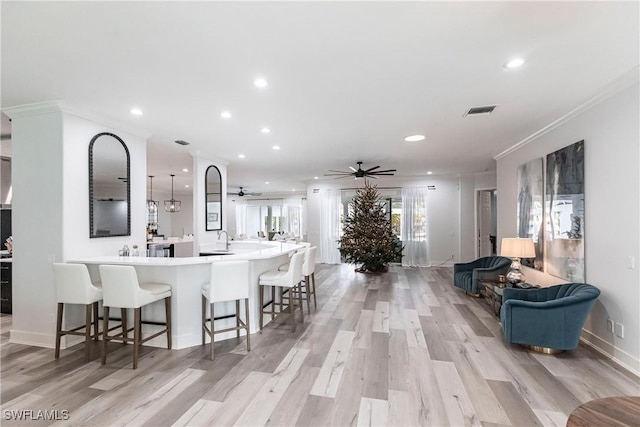 kitchen featuring a kitchen breakfast bar, light wood-type flooring, hanging light fixtures, and crown molding