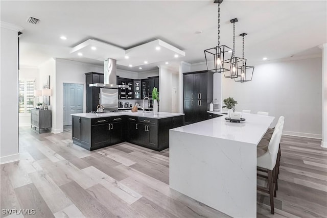 kitchen with hanging light fixtures, a spacious island, range hood, and light hardwood / wood-style flooring