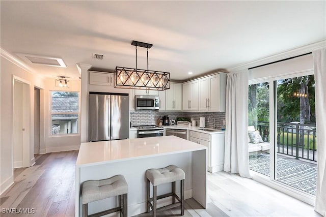 kitchen with sink, stainless steel appliances, a kitchen breakfast bar, light hardwood / wood-style flooring, and decorative light fixtures