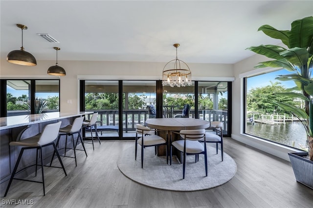 dining room featuring hardwood / wood-style flooring, a healthy amount of sunlight, a water view, and a chandelier