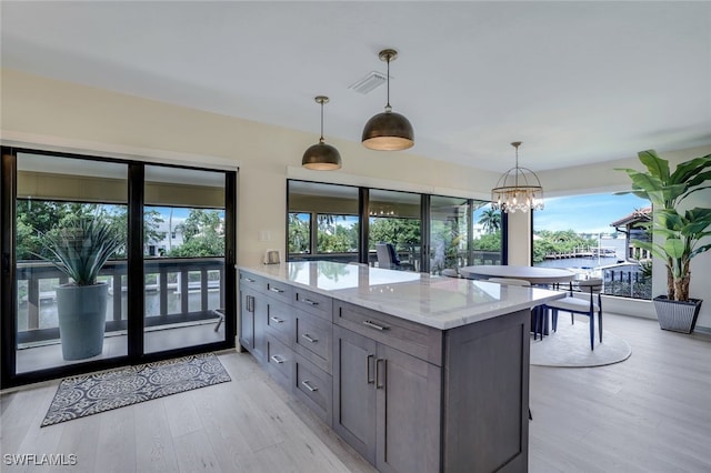 kitchen featuring hanging light fixtures, light wood-type flooring, light stone counters, and plenty of natural light