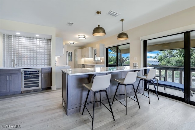 kitchen with white cabinetry, beverage cooler, hanging light fixtures, decorative backsplash, and light wood-type flooring