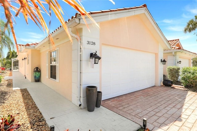 view of side of property with driveway, stucco siding, an attached garage, and a tile roof