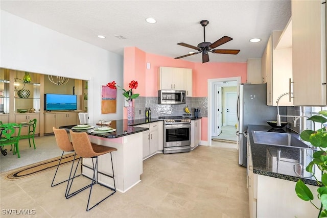 kitchen featuring a peninsula, stainless steel appliances, ceiling fan, decorative backsplash, and white cabinets