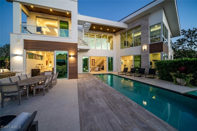 rear view of property with a patio area, outdoor dining space, an outdoor pool, and stucco siding