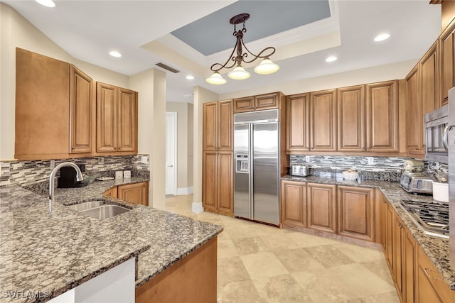 kitchen with appliances with stainless steel finishes, backsplash, a raised ceiling, sink, and decorative light fixtures