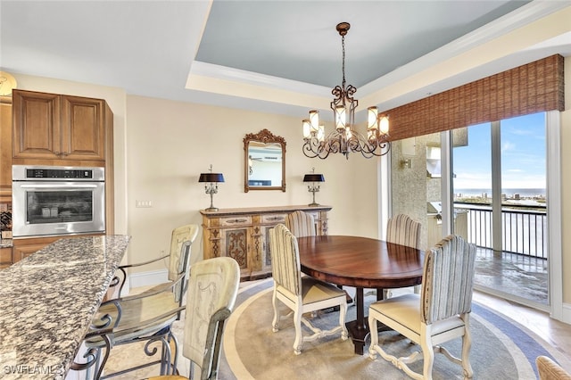 dining space featuring a tray ceiling, ornamental molding, light wood-type flooring, and an inviting chandelier