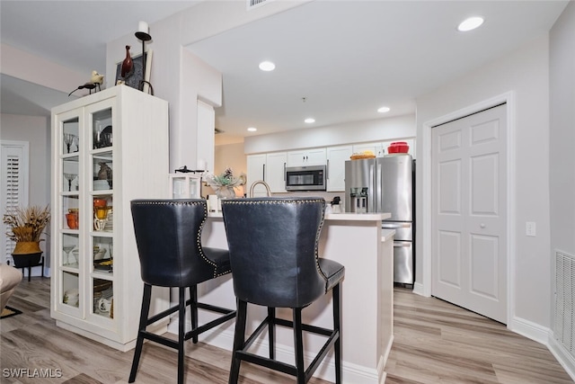 kitchen featuring a kitchen breakfast bar, kitchen peninsula, light wood-type flooring, white cabinetry, and stainless steel appliances