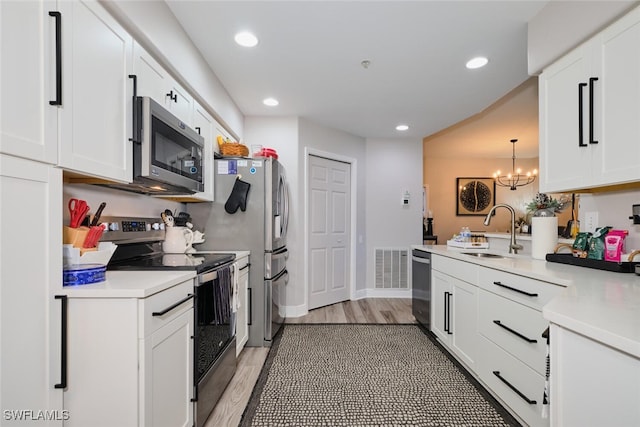 kitchen featuring sink, stainless steel appliances, a notable chandelier, white cabinets, and light wood-type flooring