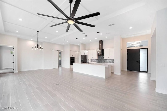 kitchen featuring a barn door, a kitchen island with sink, pendant lighting, and wall chimney range hood