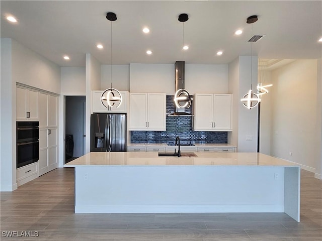 kitchen featuring fridge with ice dispenser, white cabinetry, sink, a large island with sink, and decorative light fixtures