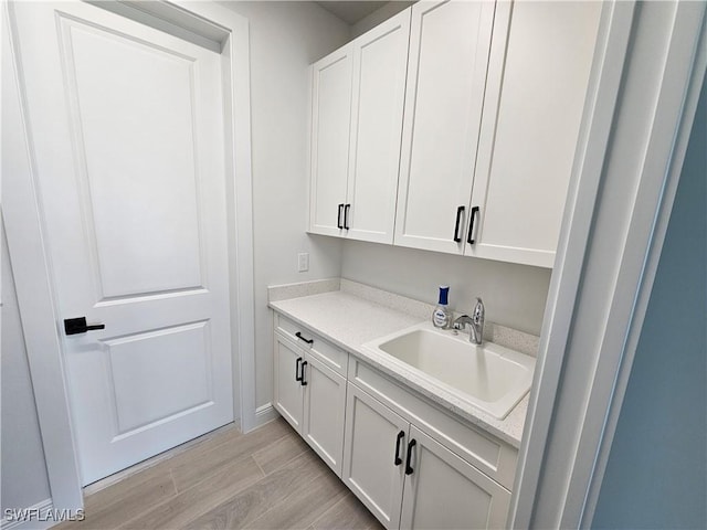 bar featuring light hardwood / wood-style flooring, white cabinetry, and sink