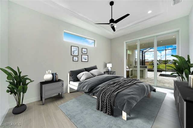 bedroom with access to exterior, light wood-type flooring, a tray ceiling, and ceiling fan