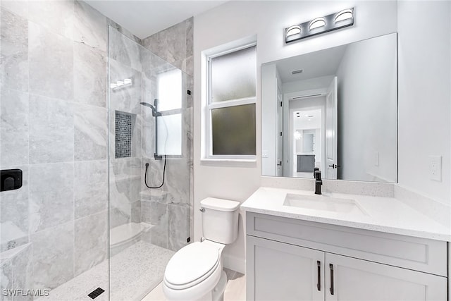 bathroom with a tile shower, vanity, and toilet