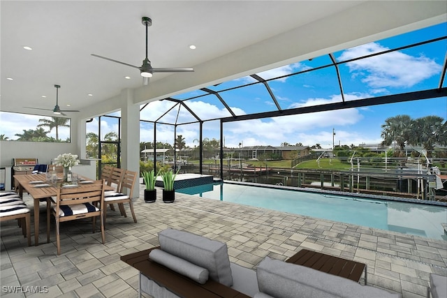 view of pool featuring glass enclosure, ceiling fan, a water view, and a patio