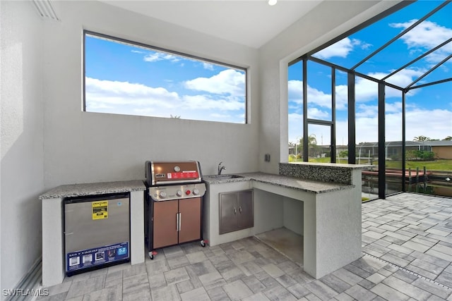 view of patio featuring a lanai, sink, and an outdoor kitchen