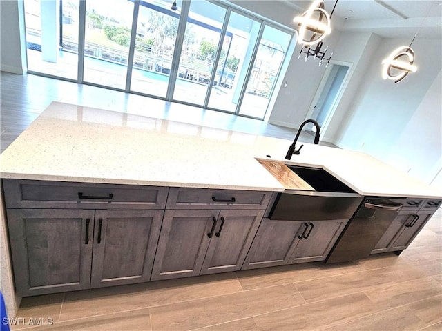 kitchen featuring sink, light hardwood / wood-style flooring, light stone countertops, dark brown cabinets, and a chandelier