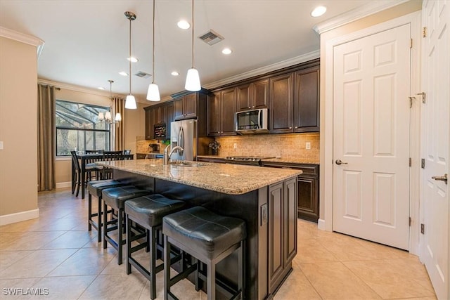 kitchen featuring dark brown cabinetry, a kitchen bar, decorative light fixtures, appliances with stainless steel finishes, and an island with sink