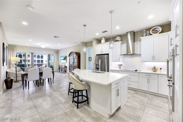 kitchen with white cabinets, stainless steel fridge with ice dispenser, a center island with sink, and wall chimney exhaust hood