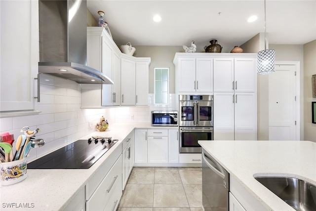 kitchen with tasteful backsplash, wall chimney exhaust hood, stainless steel appliances, white cabinets, and hanging light fixtures